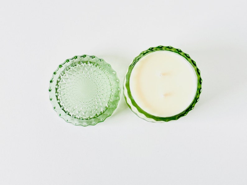 K&ouml;nnte beinhalten: Ein gr&uuml;nes Glas-Kerzengef&auml;&szlig; mit Deckel. Die Kerze ist wei&szlig; und hat zwei Dochte.