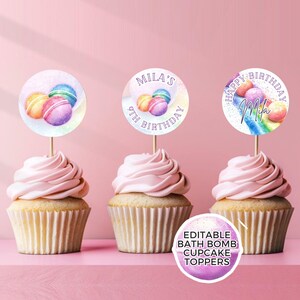 May include: Three cupcakes with pink frosting topped with round cupcake toppers. The toppers feature a watercolor design of macarons and a rainbow. The text on the toppers reads "Mila's 9th Birthday" and "Happy Birthday Mila".