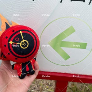 May include: A plush toy shaped like a clock with flames. The clock face is red with black details and yellow hands. The toy is held in front of a sign with a green arrow.