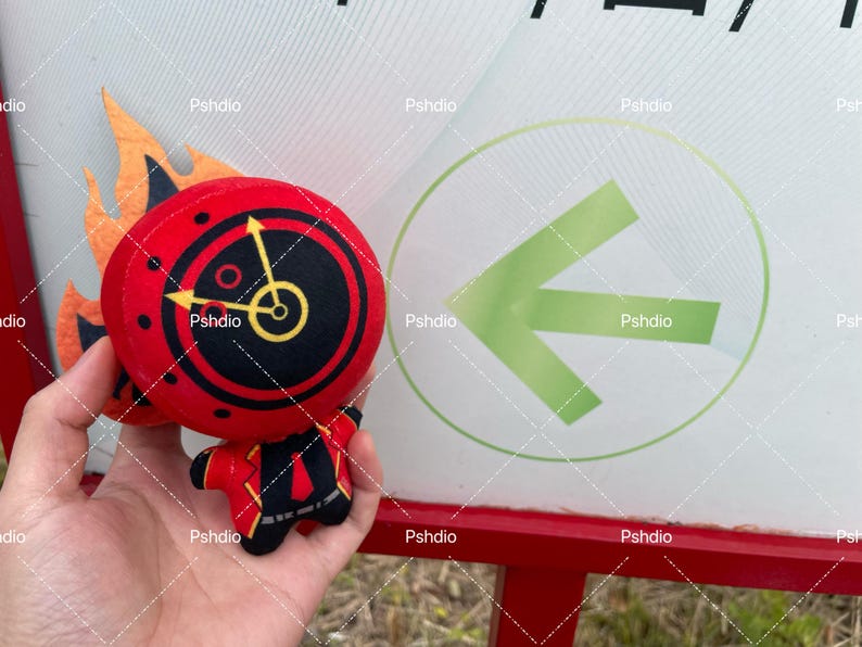 May include: A plush toy shaped like a clock with flames. The clock face is red with black details and yellow hands. The toy is held in front of a sign with a green arrow.