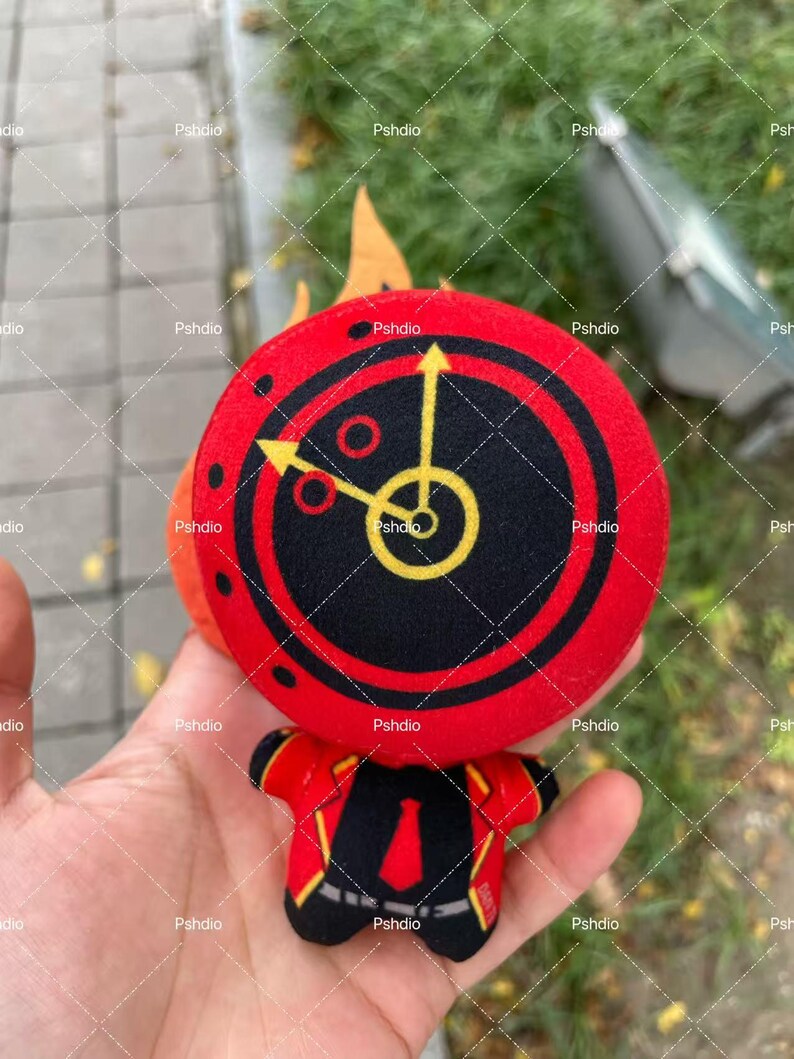 May include: A plush toy featuring a red and black circular design with yellow arrows and a central clock face. The toy has a red jacket with black lapels and a red tie. The toy is held in a hand.