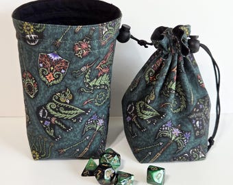 May include: Two fabric drawstring pouches in a dark teal color featuring a repeating pattern of dragons, shields, and axes with floral accents. Five multi-faceted polyhedral dice in shades of green and black are arranged in front of the bags.