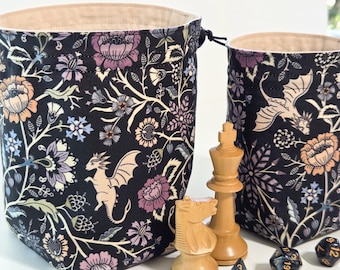 May include: Two fabric drawstring pouches featuring a black background with a floral and dragon pattern in shades of purple, peach, and cream. The pouches have a light beige interior lining and are displayed with wooden chess pieces and dice.