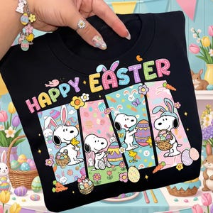 May include: Black sweatshirt with the words "HAPPY EASTER" in colorful letters. The design features Snoopy characters with Easter eggs and bunny ears. The sweatshirt has a crew neck.