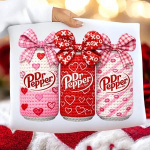 May include: A decorative pillow featuring three Dr Pepper cans adorned with crochet cozies and bows. The cans are wrapped in pink, red, and white crochet with heart and lip designs. Each can has a bow on top, with the text "Dr Pepper Est. 1885".