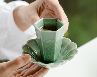 May include: A green ceramic teacup with a hexagonal shape and a matching saucer with a scalloped edge. The cup is filled with tea.
