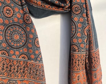 May include: A teal and orange patterned scarf. The scarf displays detailed floral and geometric patterns. The borders and sections of the scarf are a deep orange, with the main body in teal. The scarf is draped.