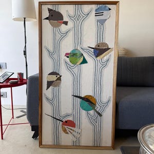May include: A rectangular framed wall art piece featuring a light-colored fabric background with embroidered blue tree silhouettes. Six stylized birds made from various fabric scraps in shades of gray, green, blue, yellow, and red are attached.