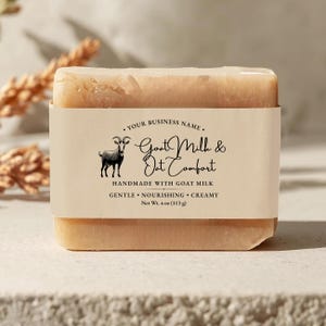 May include: A rectangular bar of soap with a beige paper label wrapped around it. The label features a goat illustration and the text "Goat Milk & Oat Comfort". The soap weighs 4 oz.