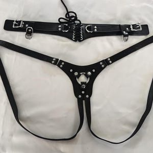 May include: Black leather harness with silver hardware and a lace-up detail. The harness has two straps that connect in the front and a single strap that connects in the back.