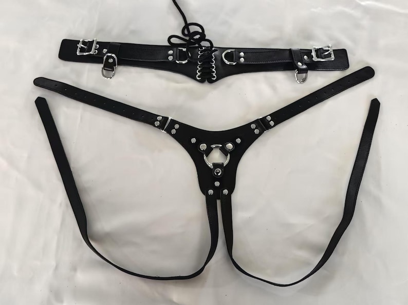 May include: Black leather harness with silver hardware and a lace-up detail. The harness has two straps that connect in the front and a single strap that connects in the back.
