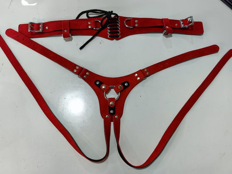 May include: Red leather harness with a metal ring and straps. The harness has a separate belt with a lace-up design.