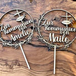 Könnte beinhalten: Zwei Holz-Kuchentopper mit einem Kreisdesign und einem Blätterkranz. Der Text auf den Toppern lautet "Zur Kommunion von Amelia" und "Zur Kommunion von Mailo".