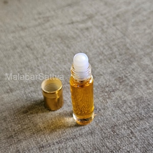 May include: A clear glass roller bottle with a gold cap and a white roller ball. The bottle is filled with a yellow liquid.