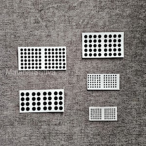 May include: Five white rectangular stickers with black dot patterns. The stickers vary in size, with the largest having a grid of dots and the smallest a smaller grid. They are arranged on a grey textured surface.