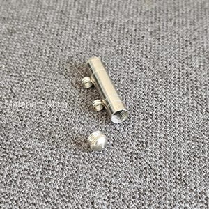 May include: A cylindrical silver-toned metal pendant or container with a screw-top lid. The main body features two small attached loops on one side and a threaded opening at the bottom. The surface is smooth and metallic with a polished finish.