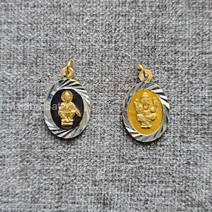 Puede incluir: Dos colgantes dorados con figuras religiosas. Cada colgante tiene forma ovalada con borde plateado y dorado. Uno presenta una figura sentada y el otro una deidad con múltiples brazos. Los colgantes están sobre una superficie gris.