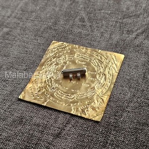 Op de afbeelding: Een zilveren amulet met drie ringen op een gouden achtergrond met ingewikkelde ontwerpen en schrift.