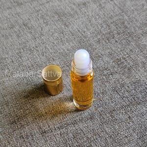 May include: A gold roller bottle with a clear glass body and a white roller ball. The bottle is filled with a yellow liquid.