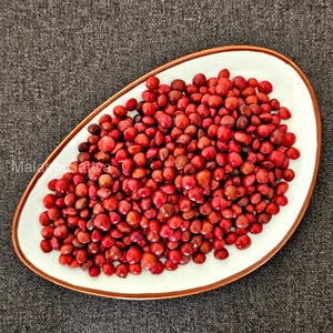 May include: A white oval plate with a brown edge, overflowing with small, red seeds. The seeds are tightly packed, creating a rich, textured surface. The plate sits on a grey surface. The image is taken from above.