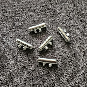 Könnte beinhalten: Fünf silberne, röhrenförmige Perlen aus Metall mit mehreren Löchern. Die Perlen sind für die Verwendung in der Schmuckherstellung gedacht.