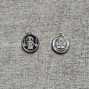 Puede incluir: Dos colgantes plateados con figuras religiosas. Uno tiene un fondo oscuro con una figura y la palabra "Satva". El otro colgante tiene una figura con un fondo radiante. Ambos colgantes tienen un diseño circular.