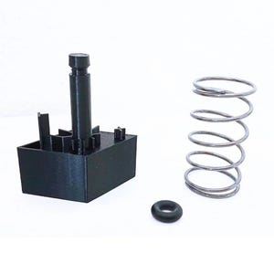 Peut inclure: Un composant en plastique noir avec un poteau cylindrique et une base rectangulaire, à côté d'un ressort en métal argenté et d'un petit joint torique en caoutchouc noir. Les éléments sont disposés sur une surface blanche, probablement à des fins mécaniques ou d'ingénierie.