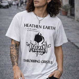 Peut inclure: T-shirt blanc avec un motif noir de crâne et le texte "HEATHEN EARTH" et "THROBBING GRISTLE". Le t-shirt comporte également la citation "...can the world be as sad as it seems?"