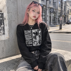 May include: A black long-sleeve sweatshirt featuring a white graphic print on the chest. The print includes the text 'STRAWBERRY SWITCHBLADE' and 'SINCE YESTERDAY' alongside a black and white illustration of two figures in polka dot clothing.