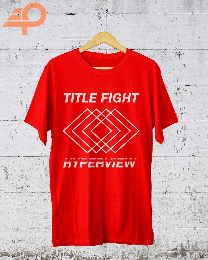 K&ouml;nnte beinhalten: Ein leuchtend rotes T-Shirt mit dem wei&szlig;en Schriftzug "TITLE FIGHT" &uuml;ber einem geometrischen Rautenmuster. Darunter steht das Wort "HYPERVIEW" in einer verzerrten Schriftart. Das T-Shirt h&auml;ngt an einem Holzkleiderb&uuml;gel.