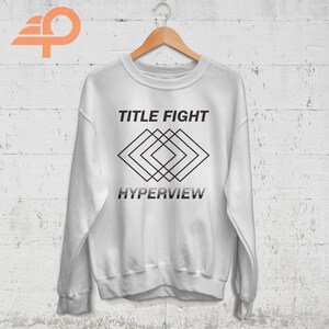 May include: White sweatshirt with black text that reads "TITLE FIGHT" and a geometric design below the text that reads "HYPERVIEW".