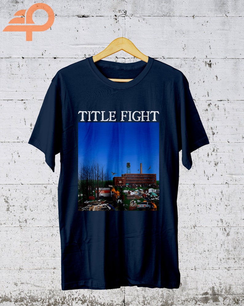 May include: A navy blue t-shirt with a graphic of a building with a blue sky and the text "TITLE FIGHT" printed in white.