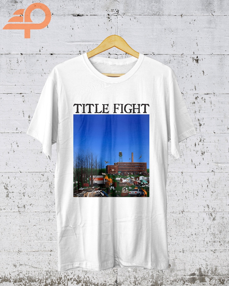 May include: White t-shirt with a blue and red graphic of a building with a blue sky and the text "TITLE FIGHT" printed in black.