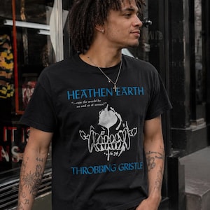 May include: A black short-sleeved t-shirt featuring the blue text HEATHEN EARTH and THROBBING GRISTLE. Below the top text is the quote ...can the world be as sad as it seems? and a white graphic illustration of a stylised skull with numbers 23 and 34.