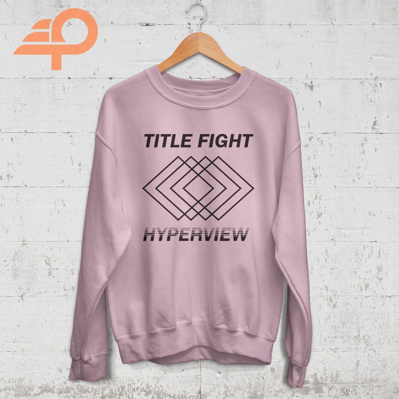 May include: A pink sweatshirt with black text that reads "TITLE FIGHT" and "HYPERVIEW". A geometric design of overlapping squares is centered on the sweatshirt.