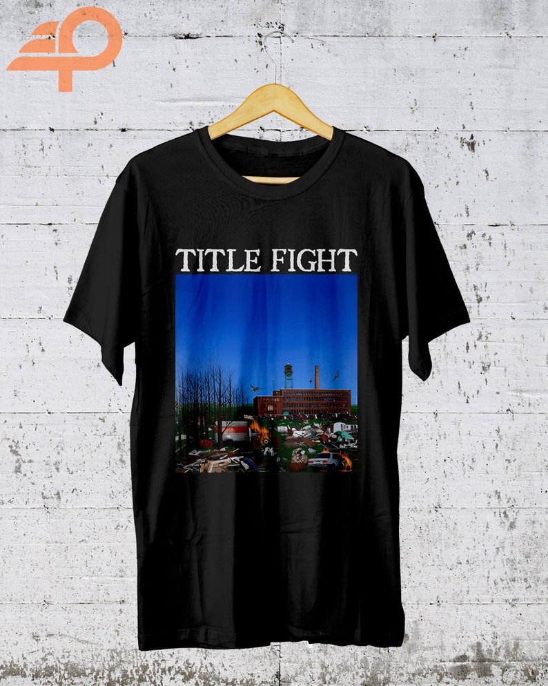 May include: Black t-shirt with the words "TITLE FIGHT" printed in white on the front. The shirt features a graphic of a building with a blue sky in the background.