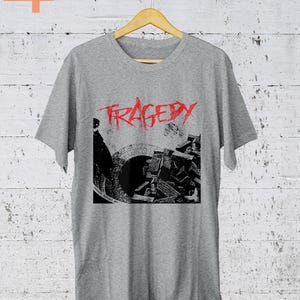 Może przedstawiać: Szary T-shirt z czarno-białym nadrukiem graficznym budynku z napisem "TRAGEDY" w czerwonych literach.