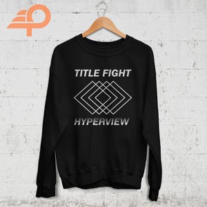 May include: Black sweatshirt with a white graphic design featuring the text "TITLE FIGHT" and "HYPERVIEW" with a geometric pattern of overlapping squares.
