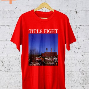 May include: Red t-shirt with a graphic print of a blue sky with a building and trees. The text "TITLE FIGHT" is printed above the graphic.