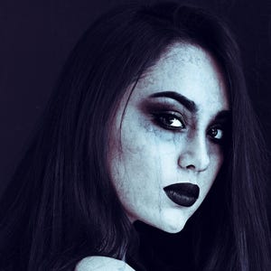 May include: A woman with dark hair and dark eye makeup looks directly at the camera. Her skin is pale and her lips are dark red.