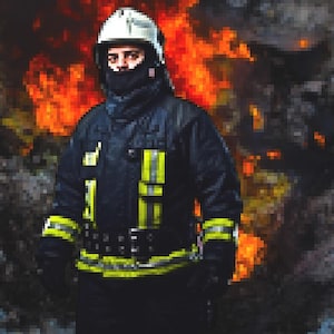 May include: A firefighter in a black and yellow fire-resistant suit and helmet stands in front of a wall of flames.