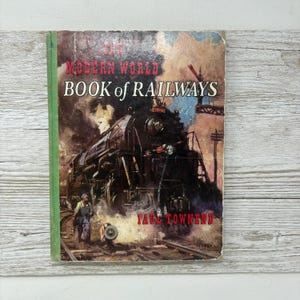 May include: A vintage book titled "The Modern World Book of Railways" with a cover illustration of a steam train. The cover shows a detailed painting of a black locomotive with smoke and a railway worker.