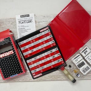 May include: A Dingbats Magnetic Pocket Edition game set, featuring a red and black game board, cards, dice, a timer, and other game pieces. The box and game board display the Dingbats logo and game instructions.