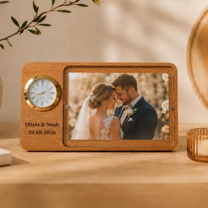 May include: Wooden photo frame with a clock and a picture of a couple. The clock has a gold-colored bezel and white face. The frame is engraved with the names "Olivia & Noah" and the date "24.08.2026".