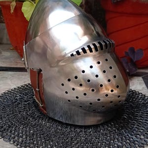 May include: A silver helmet with a visor and a chainmail coif. The helmet has a pointed top and a series of holes around the face.