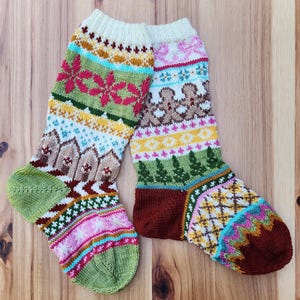 Puede incluir: Un par de calcetines de punto coloridos con patrones intrincados. Los calcetines presentan una variedad de diseños, incluyendo motivos florales, geométricos e inspirados en la naturaleza en tonos de verde, rosa, marrón y amarillo. Los calcetines se muestran sobre una superficie de madera.