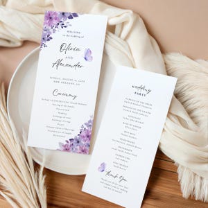 May include: Wedding ceremony and reception programme cards with a watercolour floral design in shades of purple and blue. The cards feature the names Olivia and Alexander, the date August 16, 2023, and the location New Orleans, LA. The ceremony card lists the order of events, including the prelude, processional, reading, exchange of vows, and recessional. The reception card lists the wedding party, including the parents of the bride and groom, the officiant, maid of honour, best man, bridesmaids, and groomsmen.