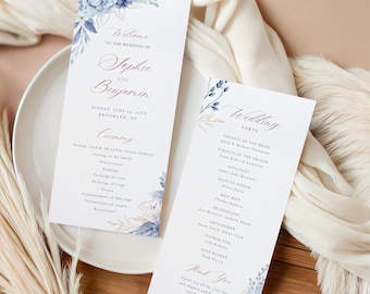 Puede incluir: Dos programas de ceremonia de boda con diseños florales en azul y dorado. Los programas incluyen los nombres de la pareja, la fecha y los detalles de la fiesta de bodas. Los programas están sobre un plato blanco.