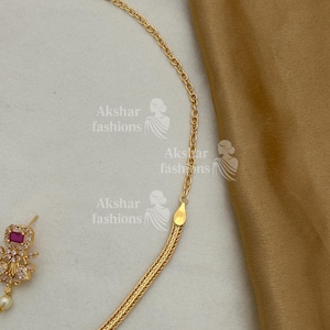 May include: A gold-coloured necklace with a woven chain design is shown in close-up. The necklace has a small, square, ruby-coloured stone pendant with a pearl drop. The image also shows a gold-coloured chain and the text "Akshar fashions".