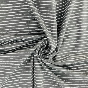 Puede incluir: Tela gris con rayas blancas horizontales de pincelada. La tela está drapeada y doblada, creando una apariencia texturizada. Las rayas tienen un aspecto ligeramente desigual, pintado a mano, añadiendo interés visual al textil.